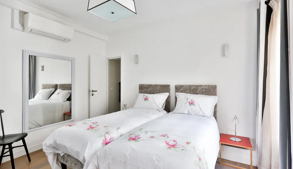 Elegant modern bedroom with twin beds, air conditioning, mirror, and floral decor. Comfort and design for your luxury property.