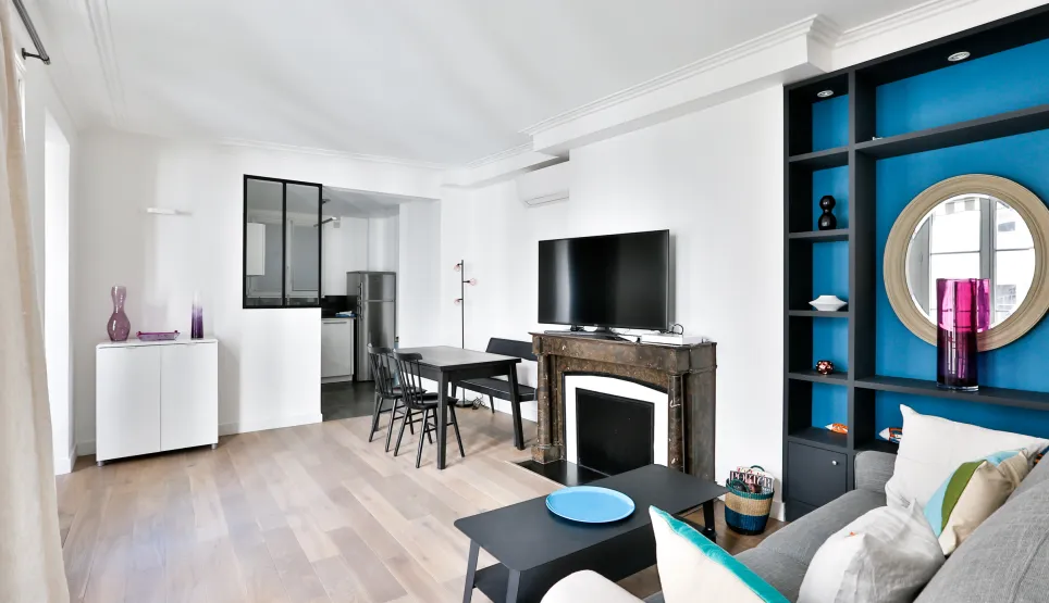Bright modern living room with open kitchen, fireplace, and vibrant blue built-in shelving. Luxury apartment design.