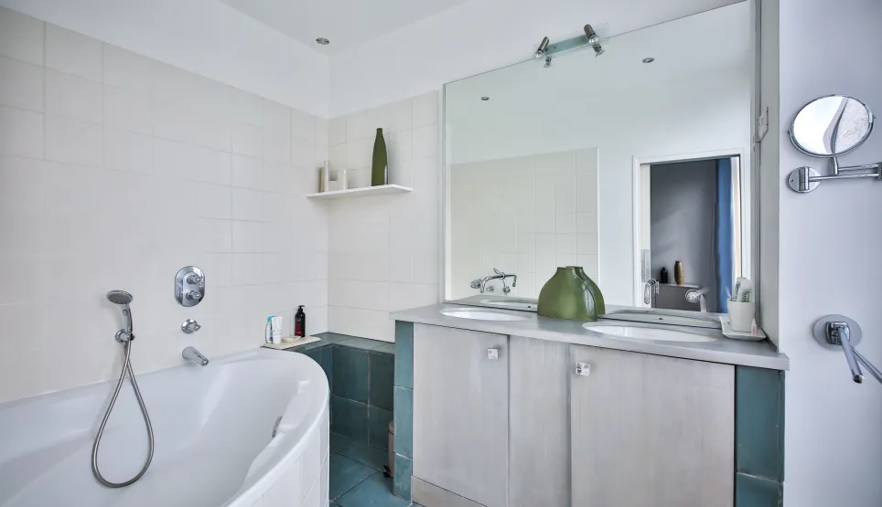 Modern luxury bathroom: bathtub, double vanity, large mirror, white/blue tiles. Sleek design, serene ambiance. Perfect for high-end property.