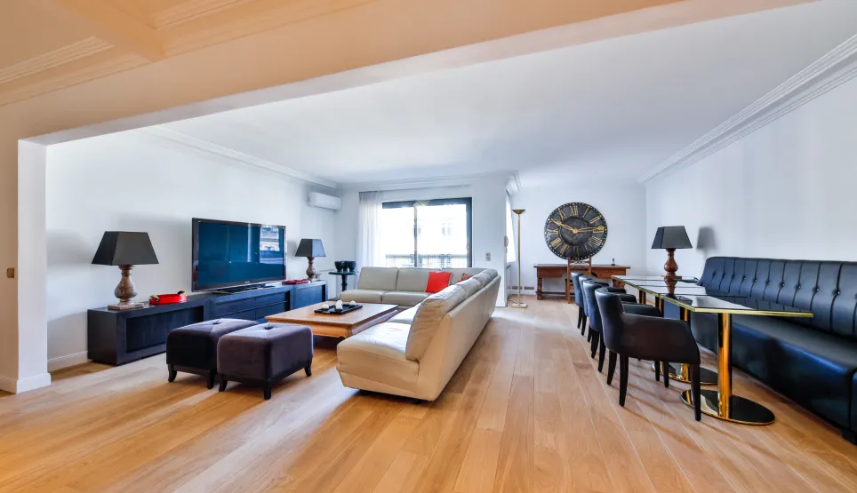 Spacious, modern living and dining room with light wood floors, designer furniture, and large TV. Perfect for a luxury apartment.