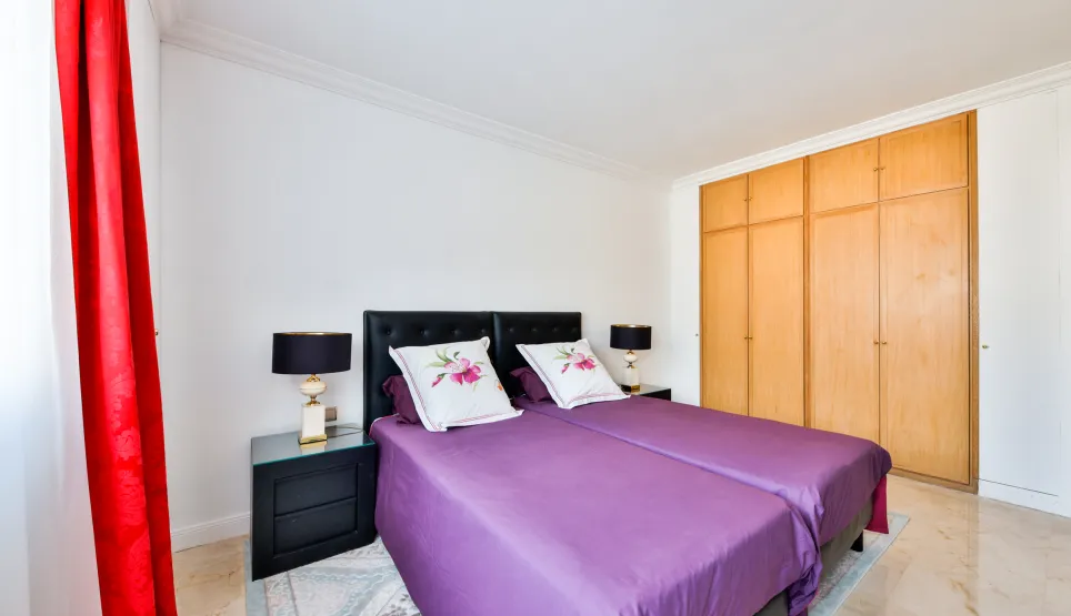 Elegant bedroom with twin beds, purple bedding, designer nightstands, and built-in wardrobes. Comfort and style for luxury property.
