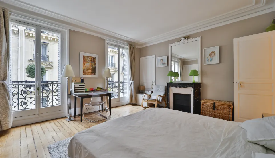 Luxury Haussmannian bedroom with balcony, hardwood floors, marble fireplace. Elegant suite, desk, moldings. Prestigious Parisian apartment.