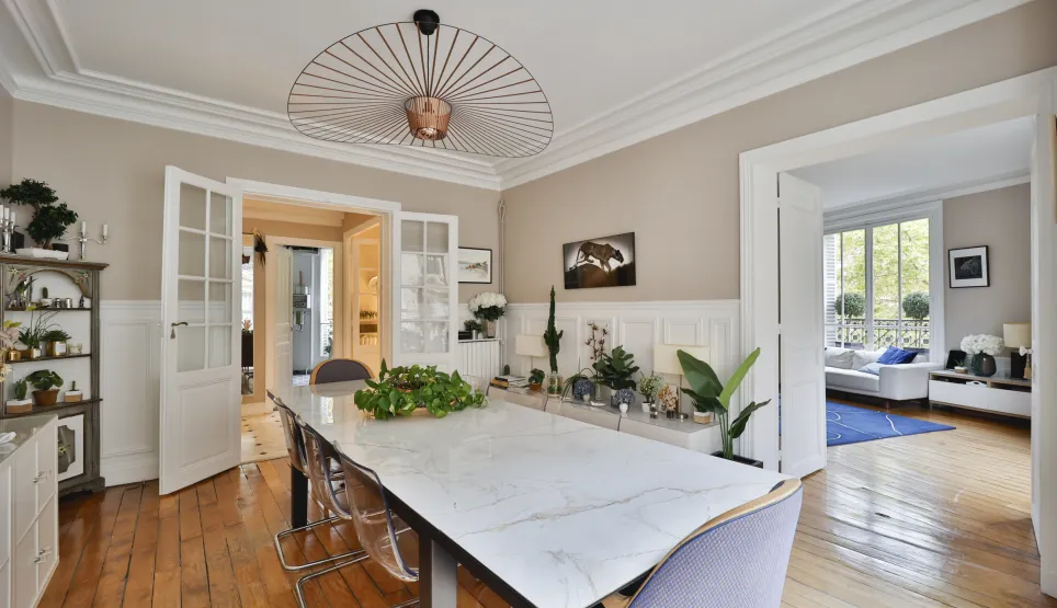 Stunning luxury dining room featuring marble table, designer chandelier, hardwood floors & moldings. Open space leading to a bright living room. Modern elegance.