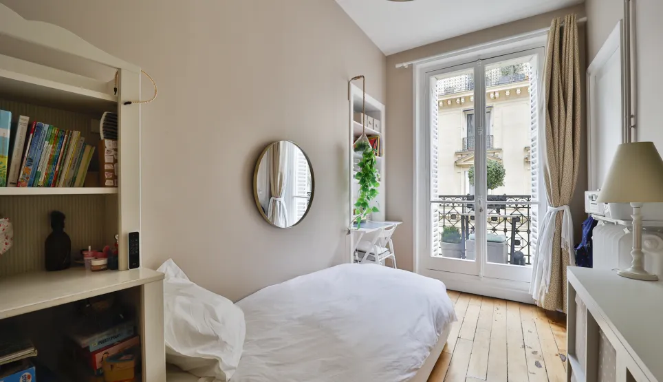 Bright Parisian bedroom with balcony, hardwood floor & city view. Single bed, built-in storage. Ideal for a child or extra office space. Charm & potential.
