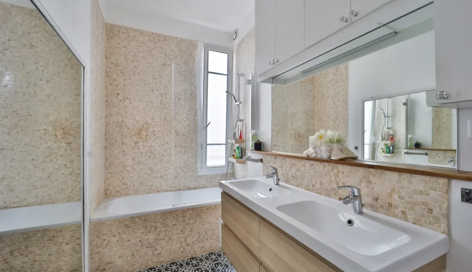 Luxurious modern bathroom featuring double vanity, bathtub, elegant tiling, and window. Refined design for a prestigious apartment.