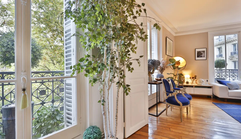 Bright luxury living room with balcony, hardwood floor & green view. Chic Parisian ambiance, elegant furniture. High-end apartment.