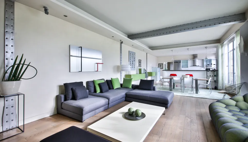 Luxury open-plan living-kitchen. Contemporary design, modular grey-green sofa, industrial beams. Bright modern ambiance for chic apartment.