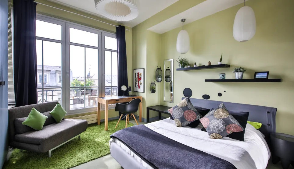 Bright modern bedroom with city view, contemporary design, comfortable bed, desk area, and lounge corner. Perfect luxury apartment.