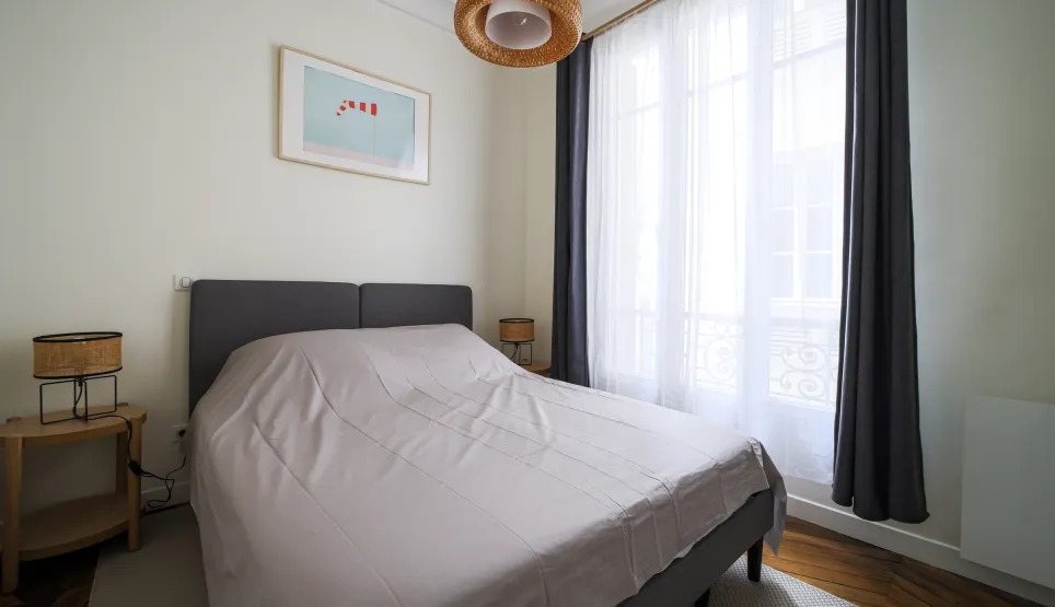 Elegant, bright bedroom with double bed, modern decor, and large window providing beautiful natural light. Perfect for a luxury apartment.