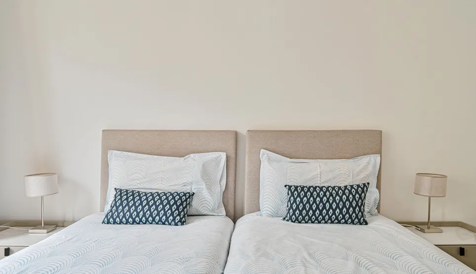 Luxury twin bedroom with elegant beige headboards, crisp white bedding, and blue accent pillows. Modern design, serene ambiance for a refined stay.
