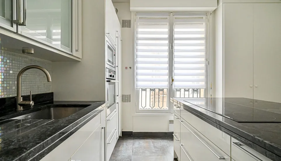 Bright, modern luxury kitchen featuring black granite countertops, integrated appliances, and large windows. Perfect for a high-end apartment.