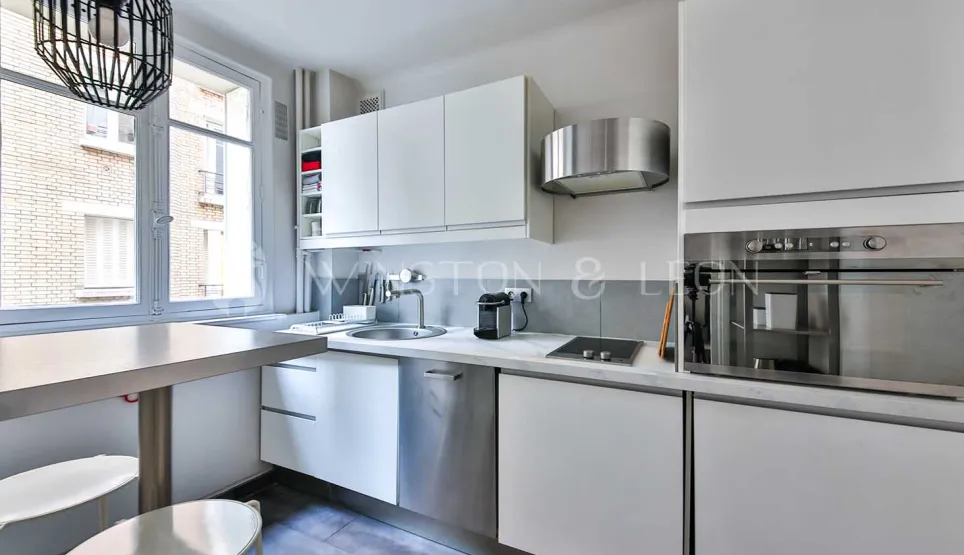 Bright modern kitchen, sleek white cabinetry, integrated stainless steel appliances, dining area. Contemporary design ideal for luxury apartment.