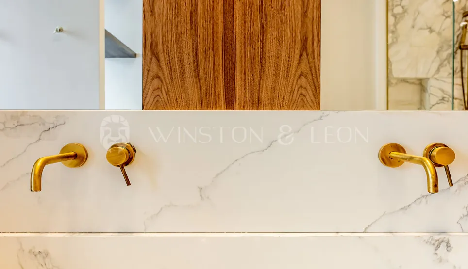 Luxury bathroom: brass wall-mounted faucets on veined white marble. Elegant contemporary design. Winston & Leon.