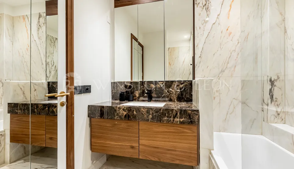 Modern luxury bathroom. Light and dark veined marble, elegant wooden vanity, and large mirror. High-end interior design.
