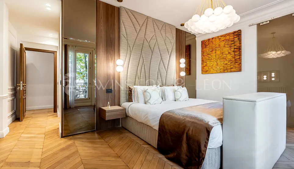 Modern luxury master bedroom: designer headboard, chevron parquet, elegant wood paneling, contemporary lighting. Refined ambiance & premium comfort.
