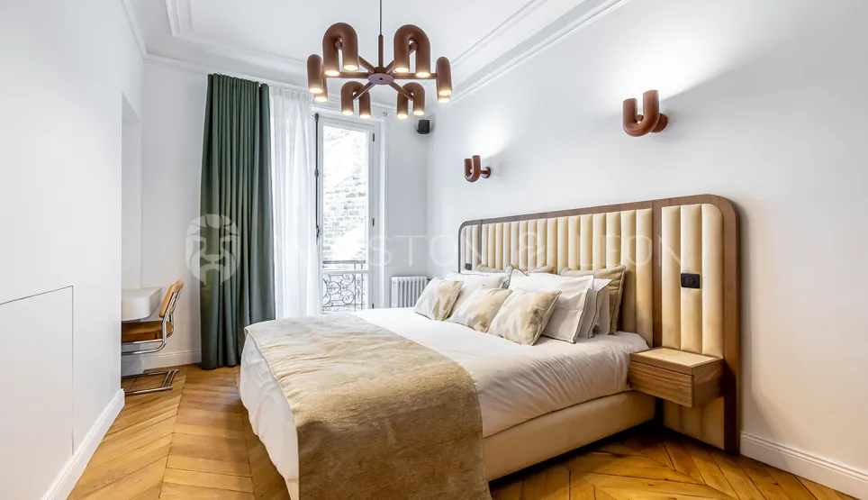 Modern luxury bedroom featuring a padded headboard, herringbone parquet, designer lighting, and balcony. Parisian elegance and comfort redefined.