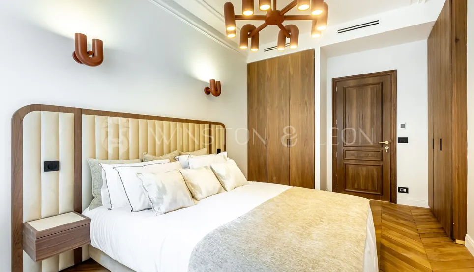 Modern luxury bedroom featuring padded headboard, designer lighting, built-in wardrobe, and parquet floor. Elegance & comfort.