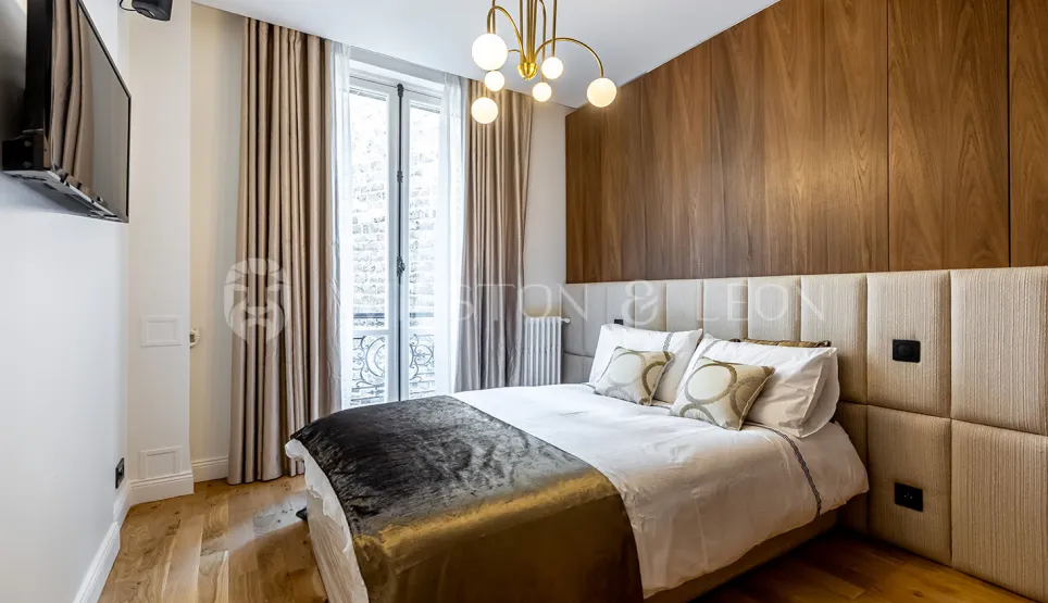 Modern luxury bedroom featuring wood paneling, padded headboard, and elegant chandelier. Contemporary design and comfort for a Parisian apartment.