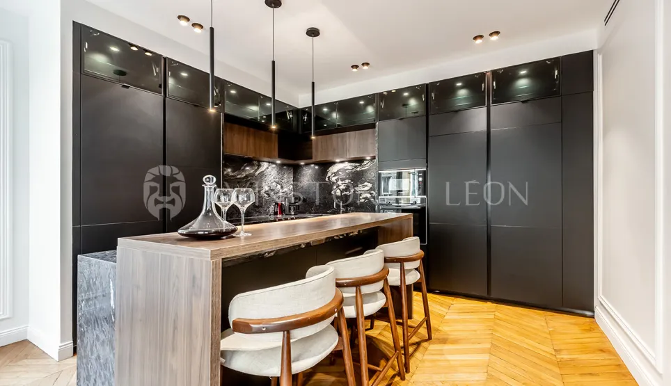 Contemporary luxury kitchen featuring a bar island, matte black finishes, light wood, marble, and parquet. Elegant & functional.