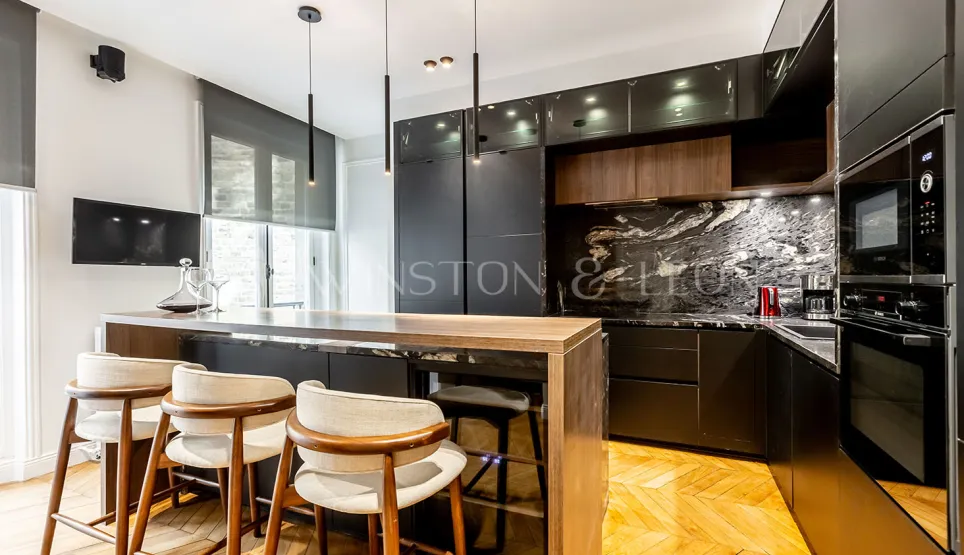 Modern luxury kitchen with wood island, veined black marble, designer stools & pendant lights.