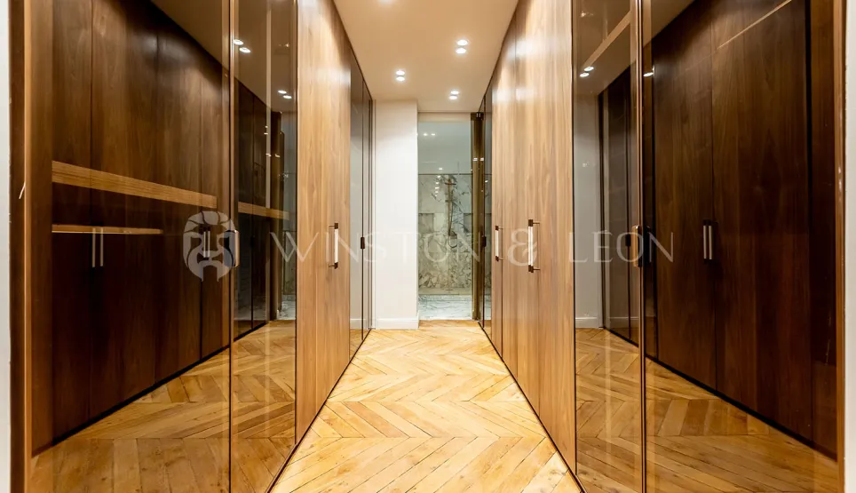 Modern luxury dressing room with wood and glass cabinets, herringbone parquet. Elegant storage for high-end property.
