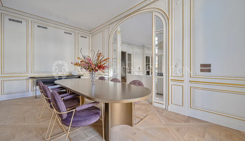 Elegant luxury Parisian dining room. Gilded moldings, parquet flooring, modern design table, velvet chairs. Haussmannian refinement.