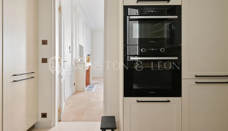 Modern Miele kitchen with integrated appliances, overlooking an elegant Haussmannian living room. Luxury apartment Paris.