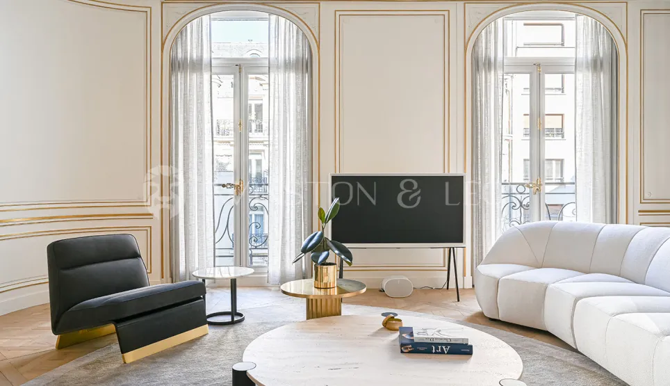 Luxury Parisian living room featuring gold moldings, contemporary designer furniture, large arched windows, and natural light. Elegant and refined.