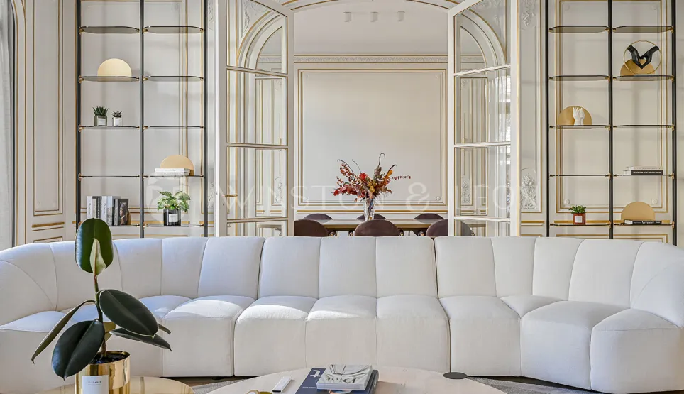 Elegant luxury living room, modern white sofa, gold moldings. Chic and refined ambiance for an exceptional Haussmannian apartment.