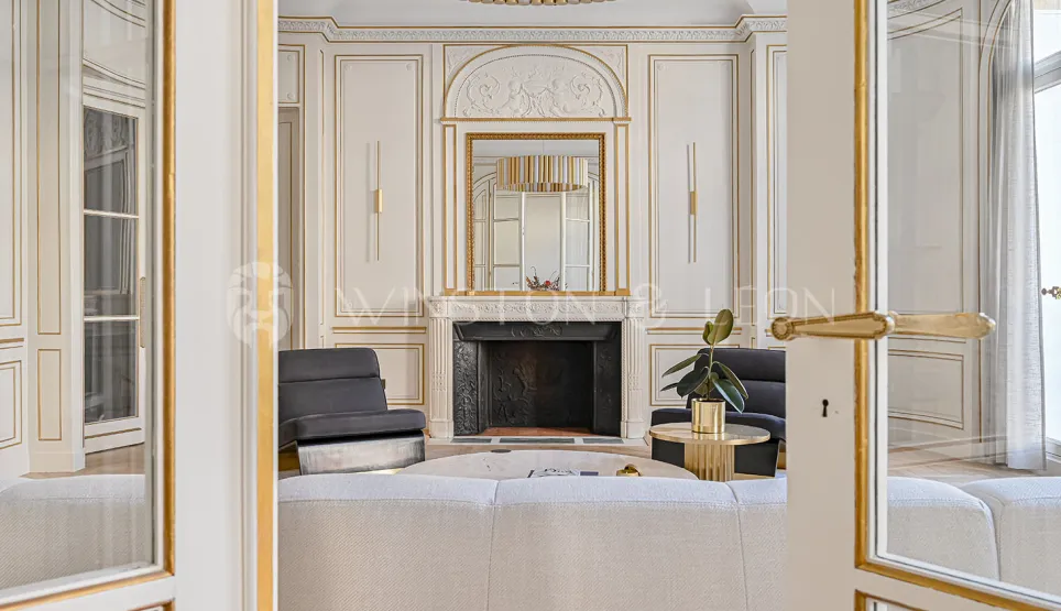Luxury Parisian living room: ornate gold paneling, classic fireplace, and elegant modern furnishings. A prestigious interior blending old charm & modern design.