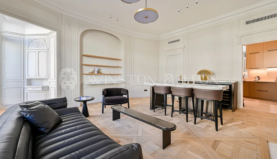 Stunning luxury Parisian living room. Contemporary design, Versailles parquet, elegant moldings, integrated bar & modern kitchen. Refined, bright ambiance.