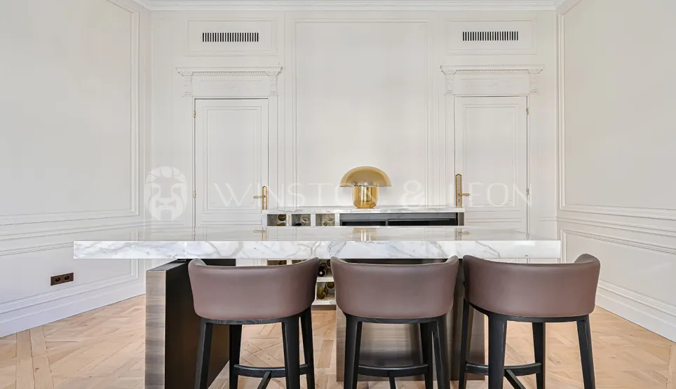 Luxury kitchen with marble island, designer stools. Elegant paneling, gold lamp. Prestige interior, chic Parisian apartment.