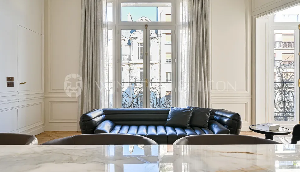 Luxury Parisian living room with black leather sofa, elegant moldings, and Haussmannian view. Contemporary design and refinement.