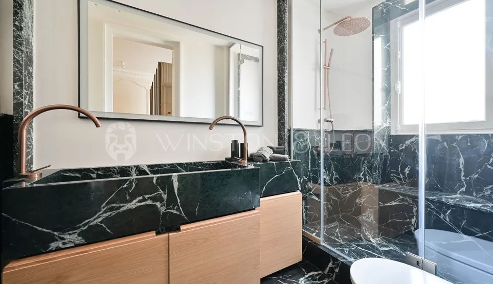 Luxury bathroom. Black veined marble, light wood double vanity, copper fixtures. Modern walk-in shower. Elegance and sophistication.