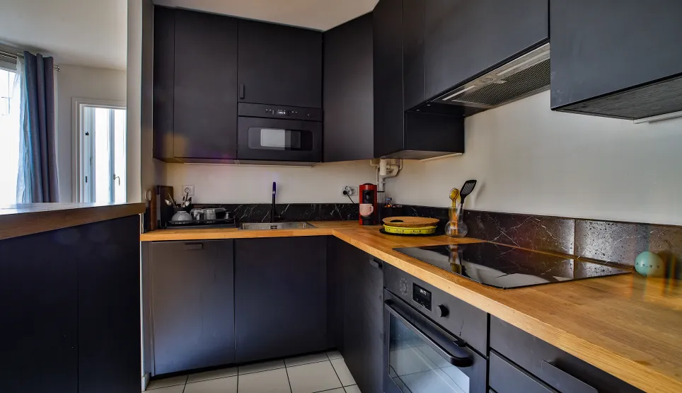 High-end kitchen, matte black cabinetry, wood countertop. Integrated appliances. Modern and luxurious ambiance.