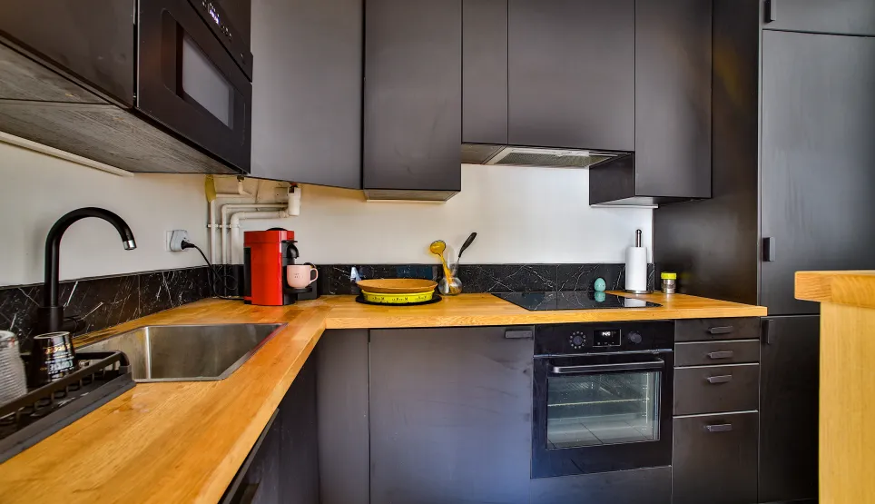 Luxury modern kitchen: matte black cabinets, light wood countertop, fully equipped. Elegant contemporary design.