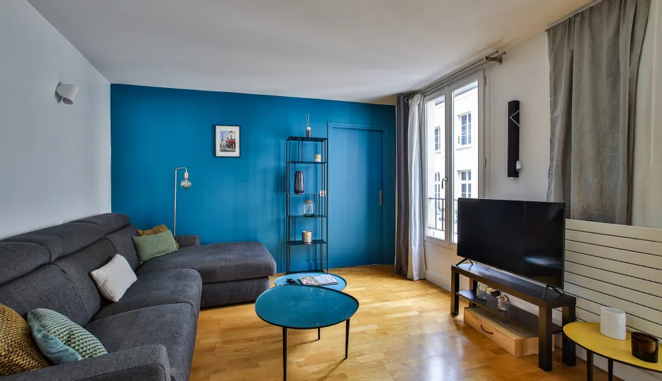 Bright modern living room with vibrant blue accent wall, grey sectional sofa, elegant hardwood floors. Perfect for a luxury apartment.