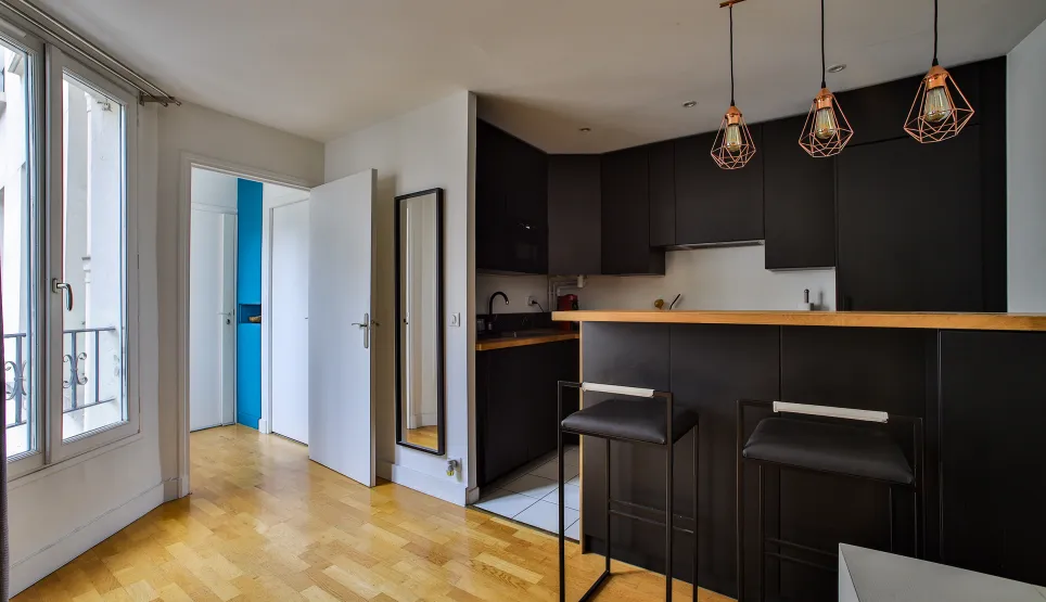 Modern black kitchen with bar, design stools, hardwood floor & copper lights. A bright and elegant living space.