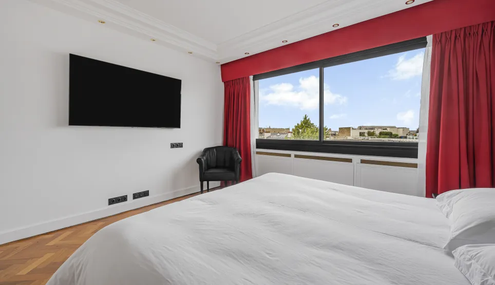 Bright, modern master suite with city views, TV, armchair, and hardwood floor. The luxury and comfort of a high-end apartment.