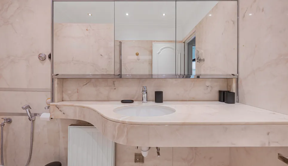 Luxurious light marble bathroom, designer sink and mirror. Refined ambiance for an exceptional property.