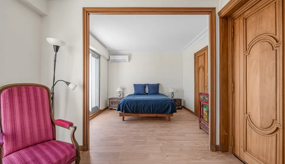 Bright, elegant master suite with blue double bed, light hardwood floors & refined furnishings. A charming luxury property interior.