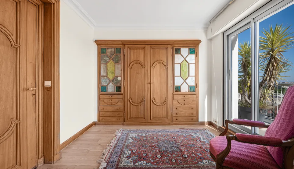 Elegant custom wooden wardrobe with stained glass, parquet floor & oriental rug. Bright terrace access. Chic & warm ambiance.