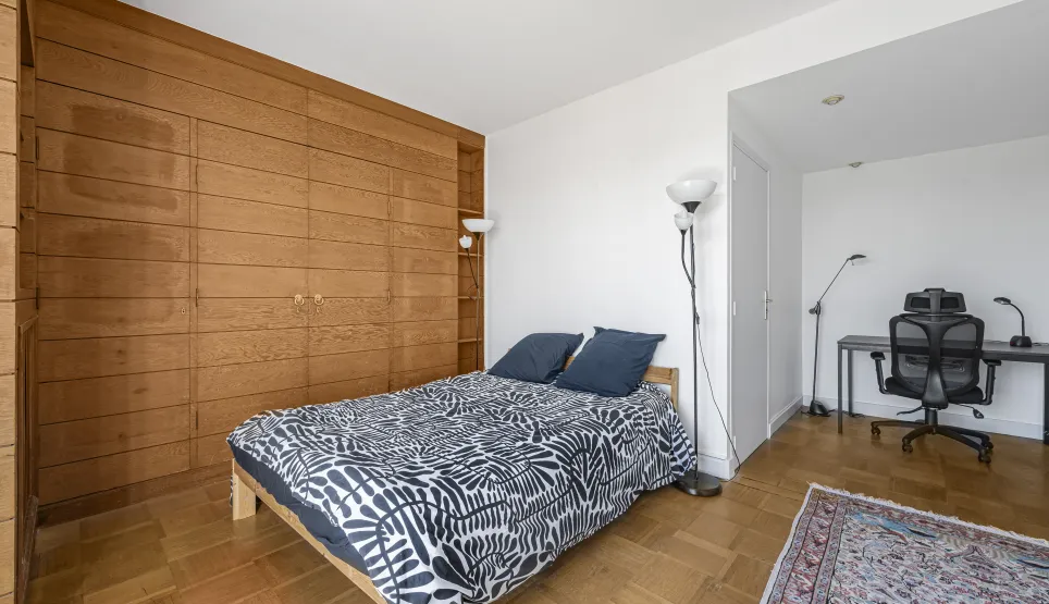Elegant bedroom featuring a large built-in wooden wardrobe, parquet flooring, and a discreet office area. Comfort and style for luxury living.