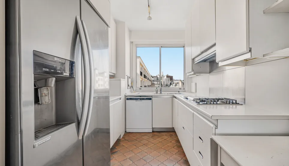 Contemporary white kitchen, fully equipped with American fridge, gas hob, and beautiful city view. Luxury and functionality.