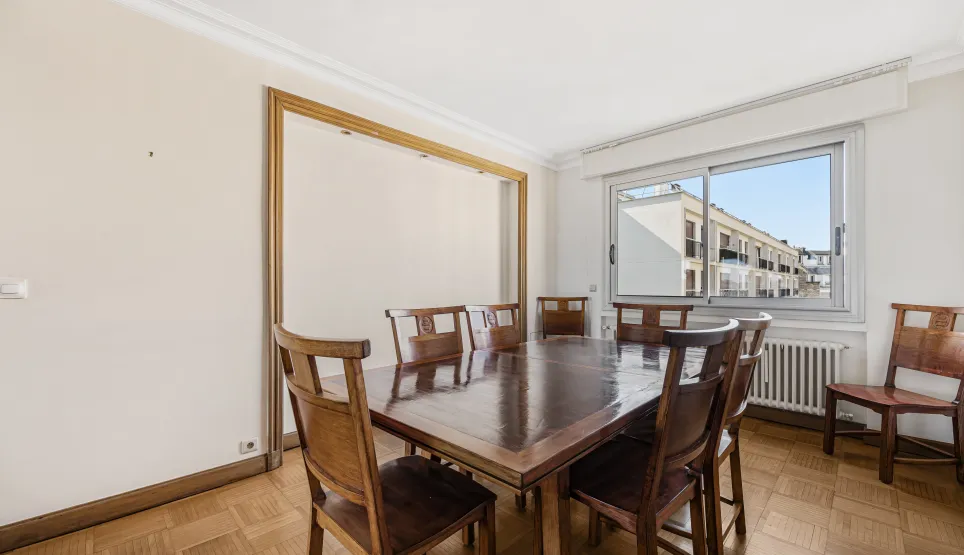 Spacious, bright dining room with parquet flooring, large solid wood table, and urban views. Perfect for a luxury apartment.