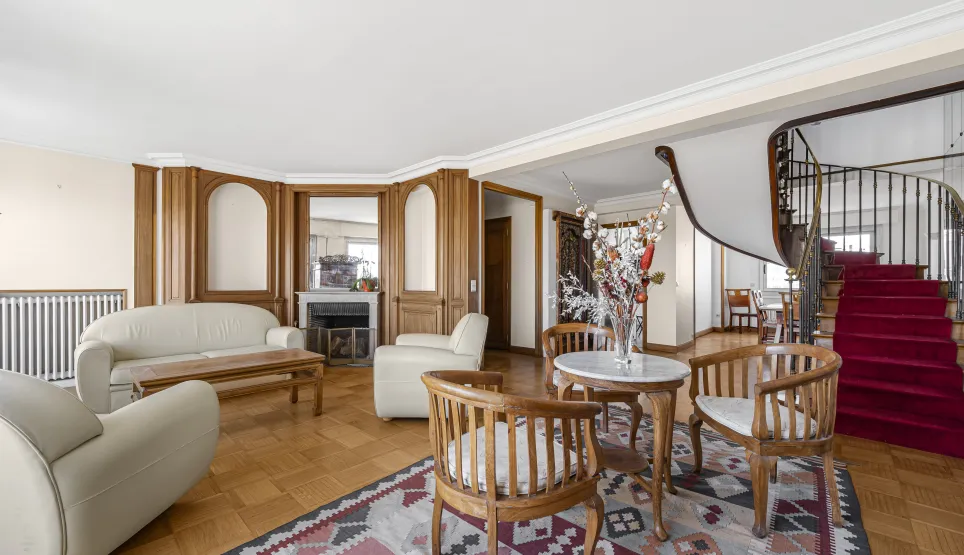 Elegant luxury living room with fireplace, wood paneling, parquet flooring, and majestic spiral staircase. Spacious property.