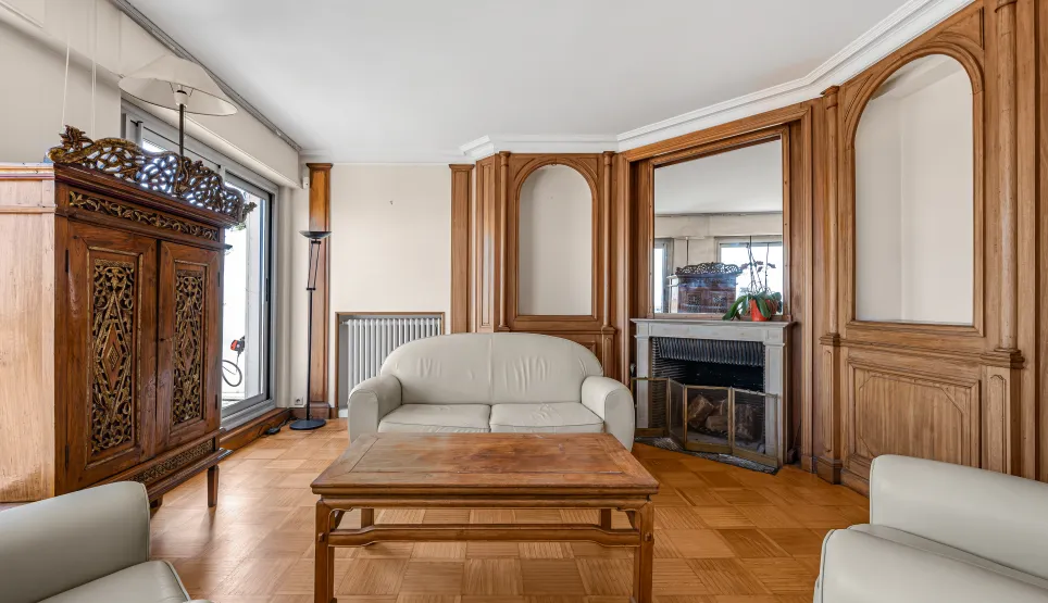 Luxury living room featuring ornate wood paneling, parquet flooring, fireplace, and classic furniture. Timeless elegance for an exceptional apartment.