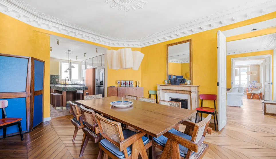 Elegant Parisian dining room with yellow walls, herringbone parquet, fireplace. Renovated luxury apartment, blending old charm & modern design.