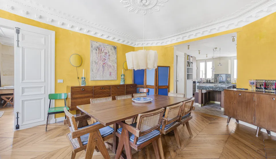 Luxury Parisian apartment: bright dining room with yellow walls, herringbone parquet, moldings. Design open kitchen. Vibrant elegance.