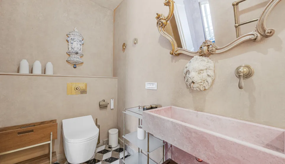 Luxury bathroom with pink marble sink, gold mirror, designer toilet and geometric tiles. Elegant and refined ambiance.